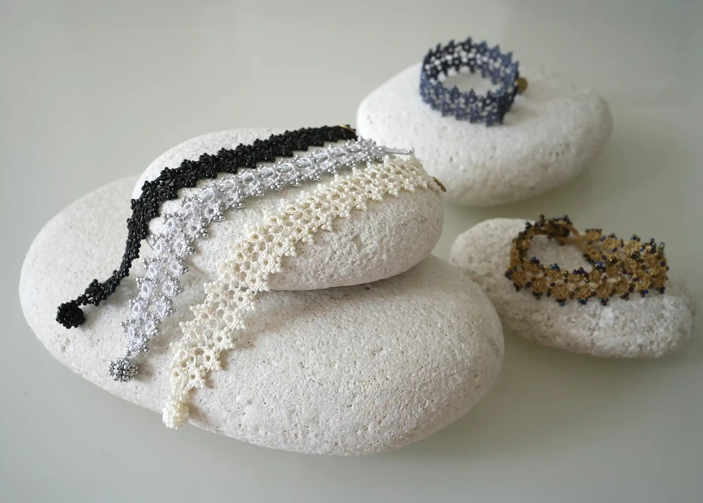 Set of handmade lace textile bracelets placed on pebbles, Husnu models, OYA collection