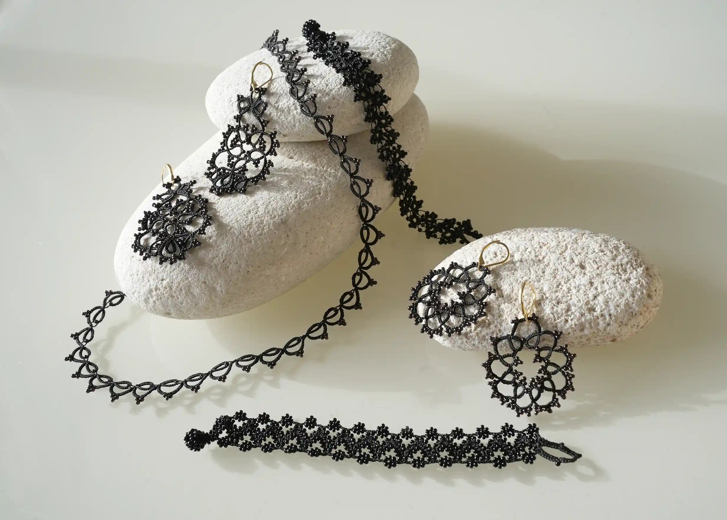 Ensemble de bijoux textiles en dentelle fait main posés sur des galets, collection OYA