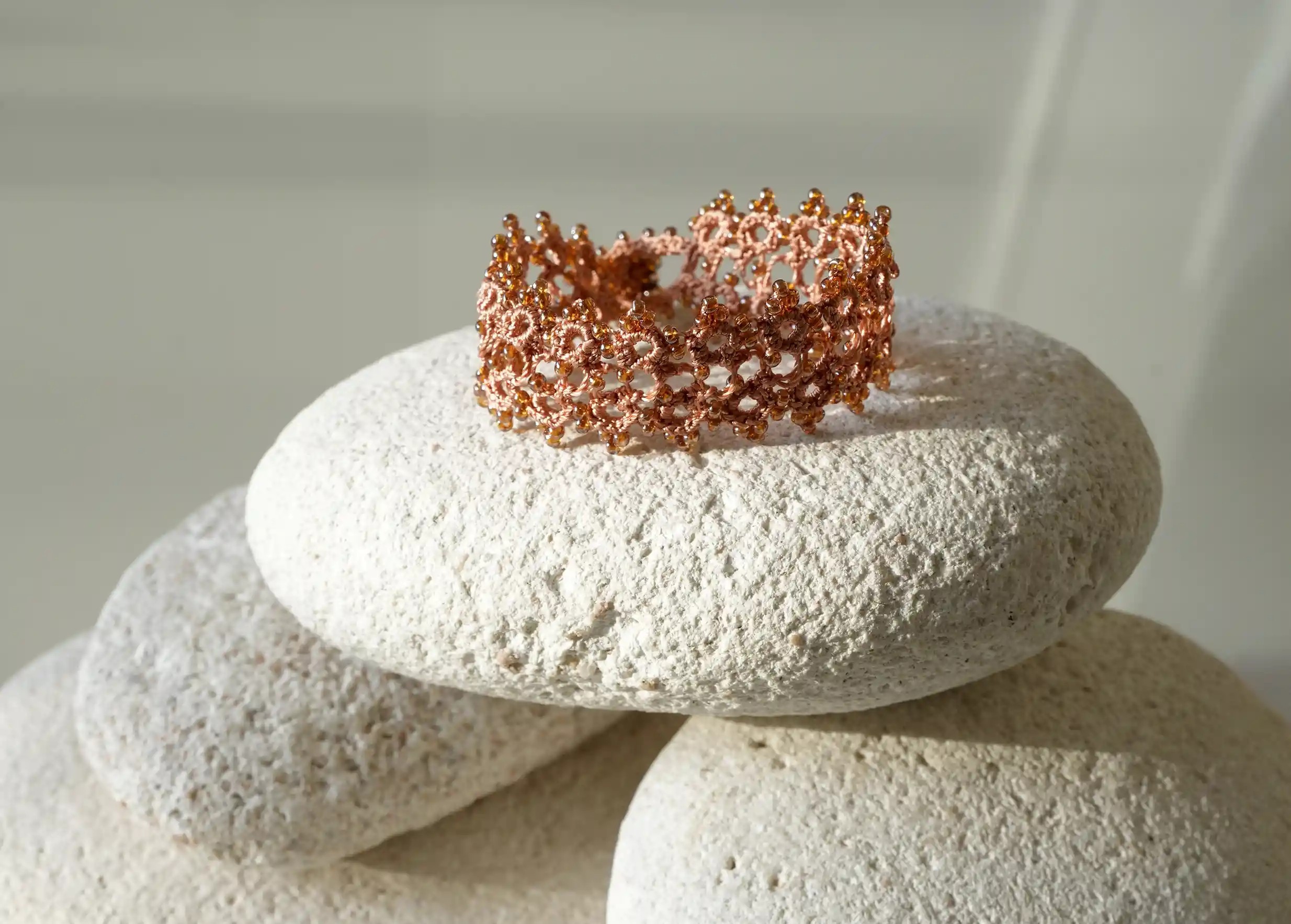 Bracelet textile en dentelle fait main,  Husnu, collection OYA, coloris orange et cuivre posé sur un galet