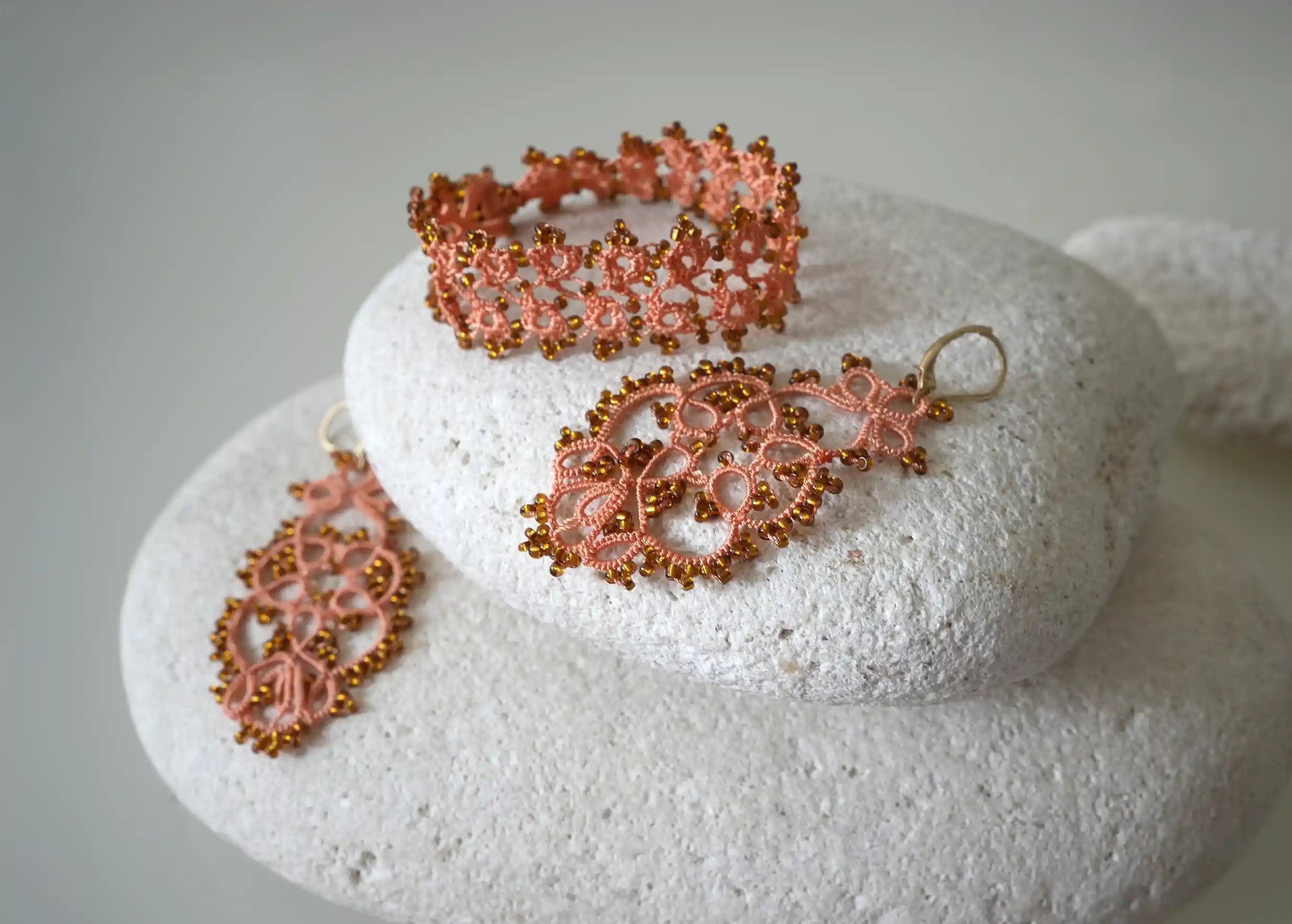 Ensemble de bijoux textiles en dentelle fait main posés sur des galets, coloris orange et cuivre, collection OYA