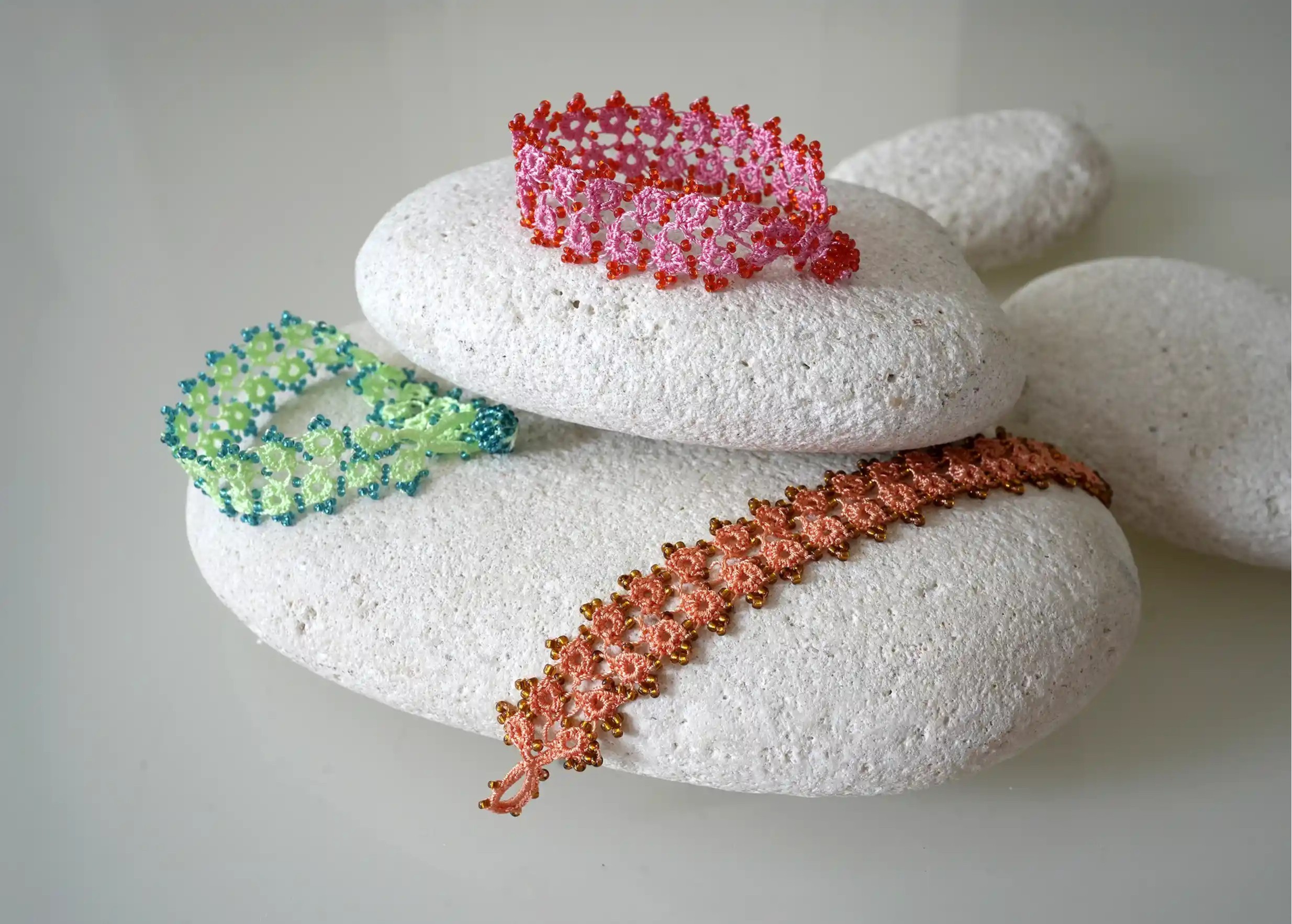 Set of handmade lace textile bracelets placed on pebbles, light colours