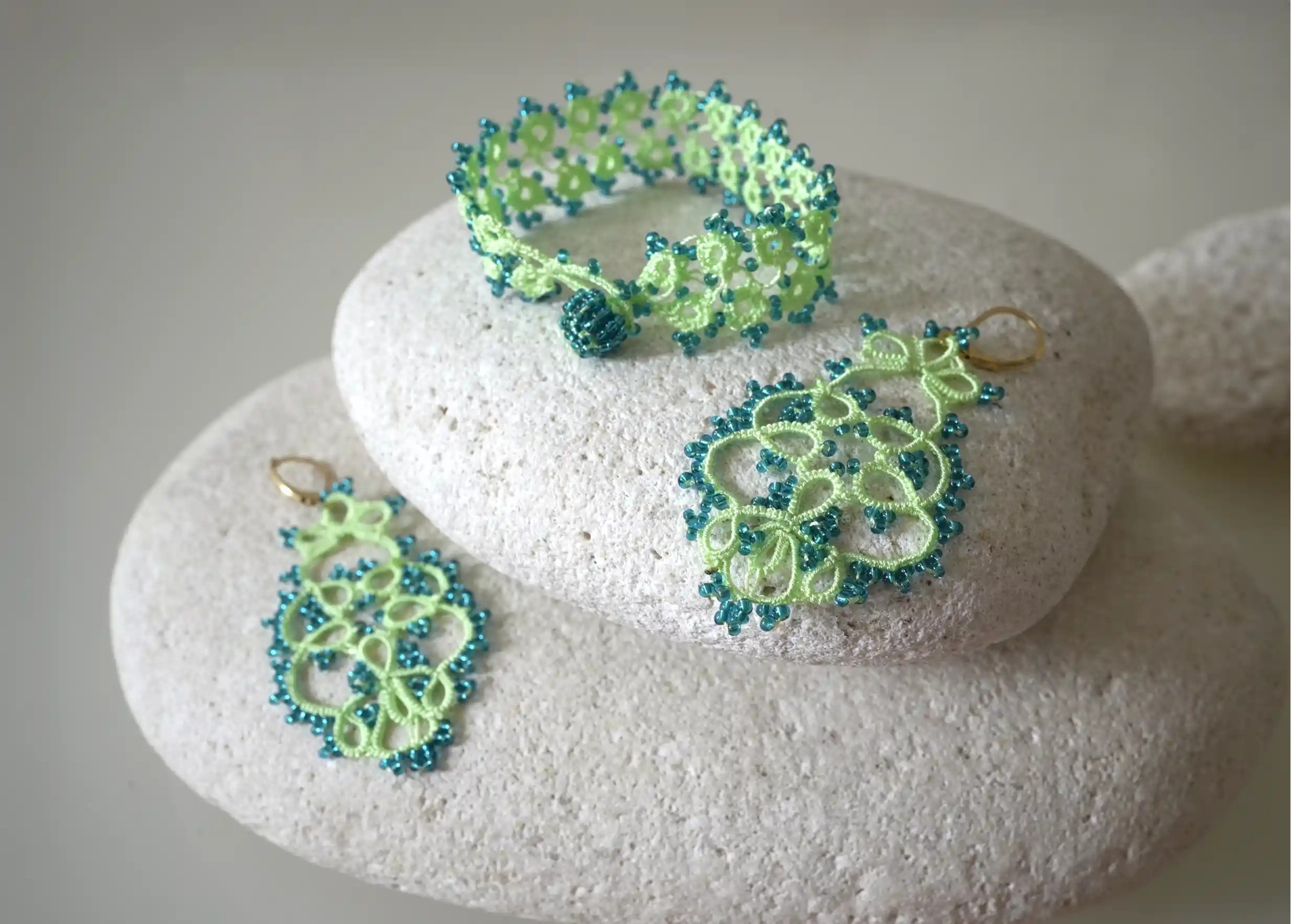 Set of handmade lace textile jewellery placed on pebbles, green and emerald colours