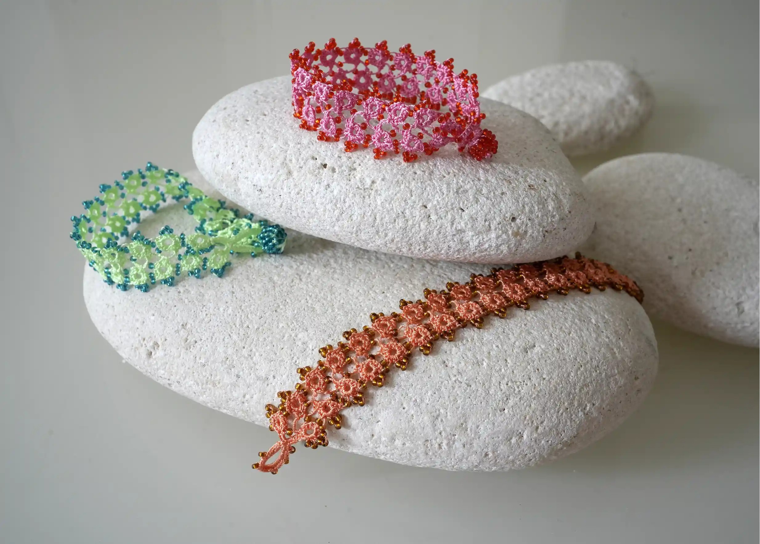 Set of handmade lace textile bracelets placed on pebbles, light colour, Karawan brand