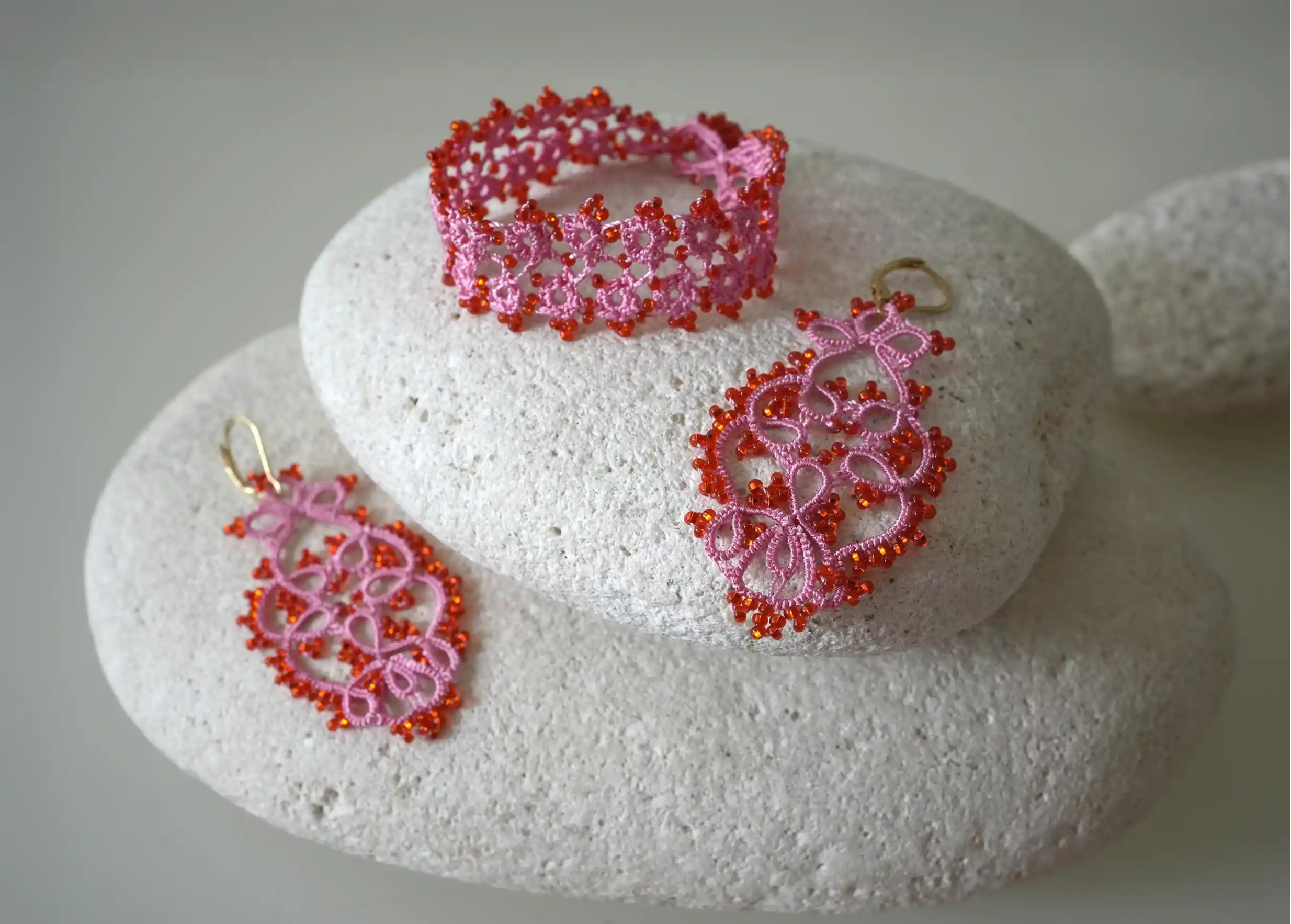 Ensemble de bijoux textiles en dentelle fait main posés sur des galets, coloris rose et rouge, collection OYA
