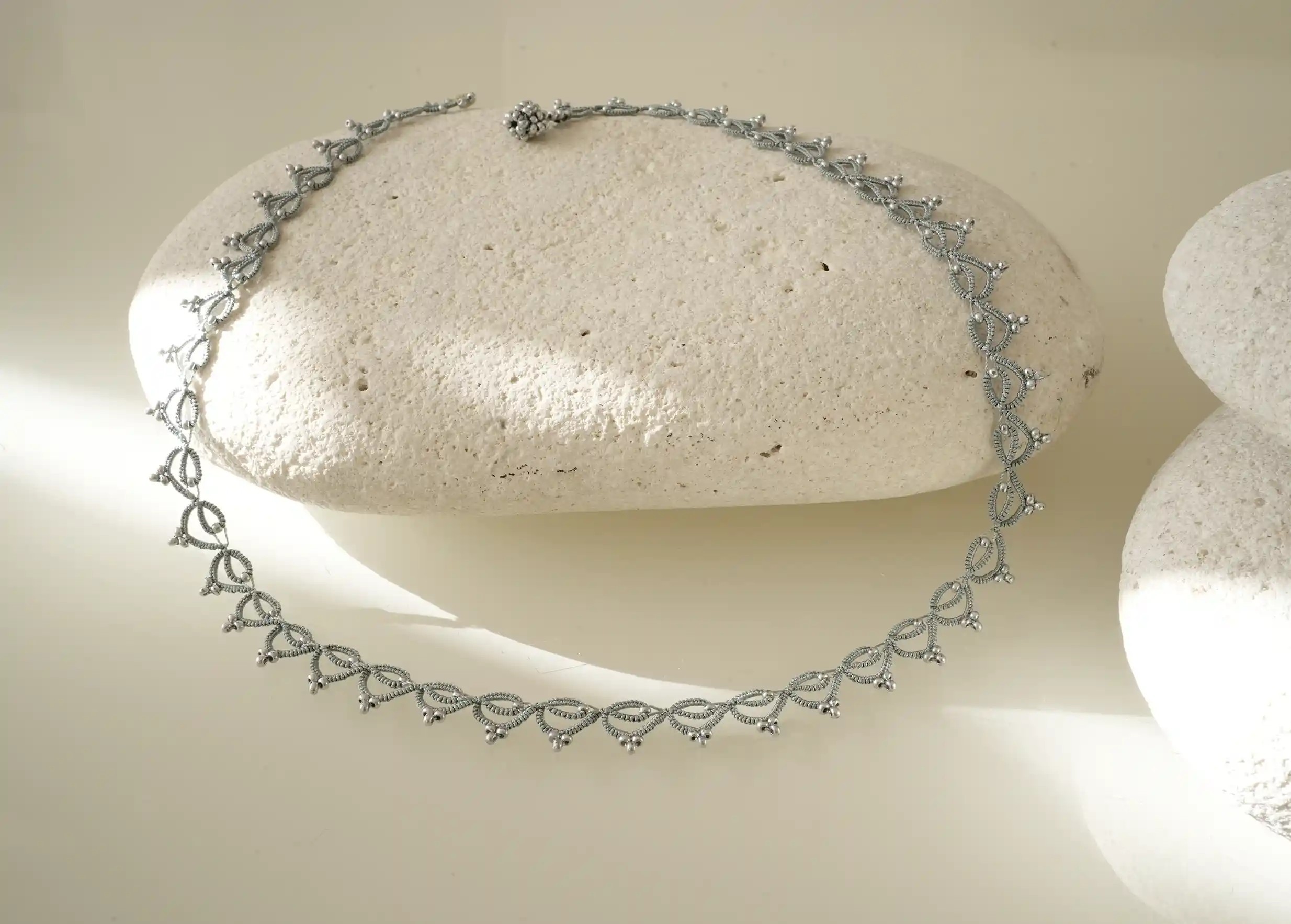 Collier tour de cou fait main en fil et perles, Lotus Chain coloris bleu glacier et argent, photo prise sur un galet