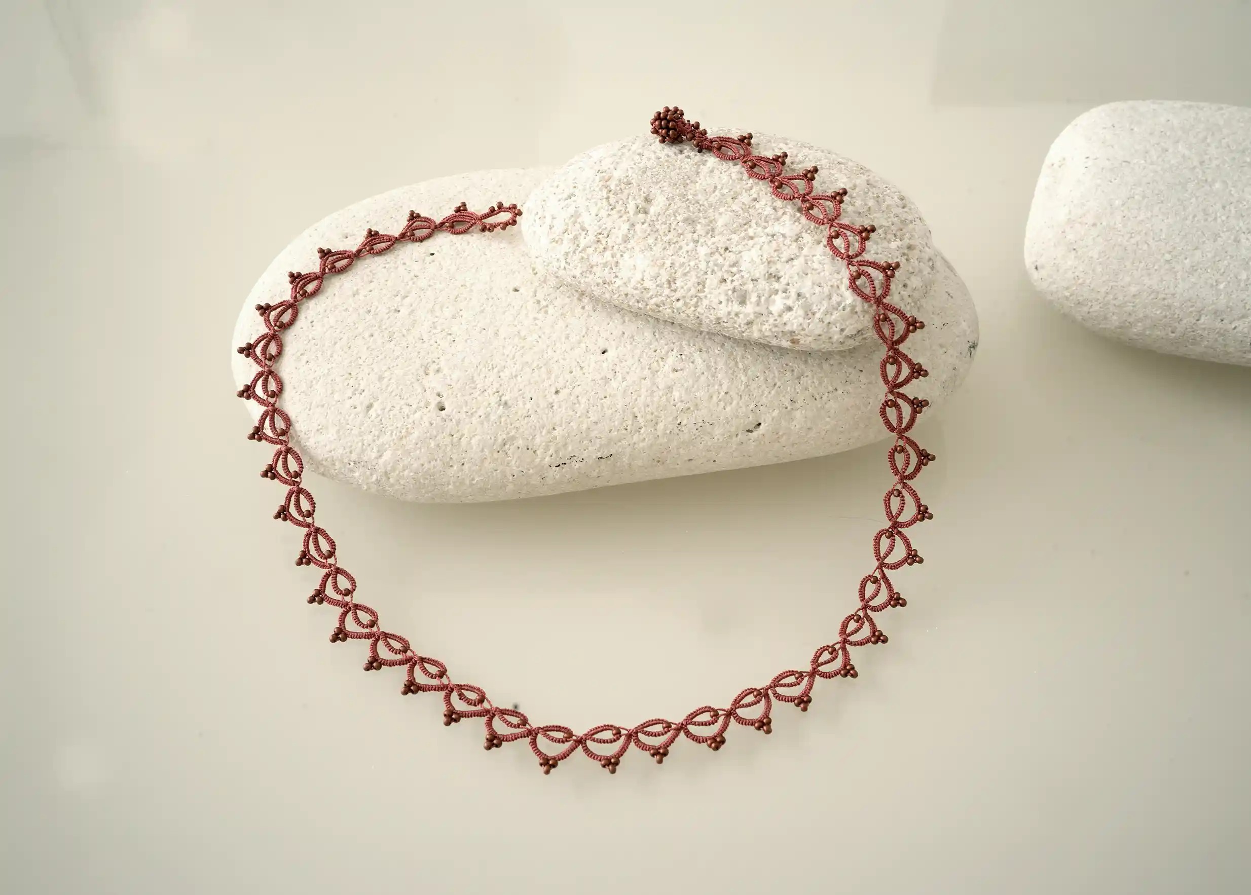 Collier tour de cou fait main en fil et perles, Lotus Chain coloris cuivre mat, photo prise sur un galet
