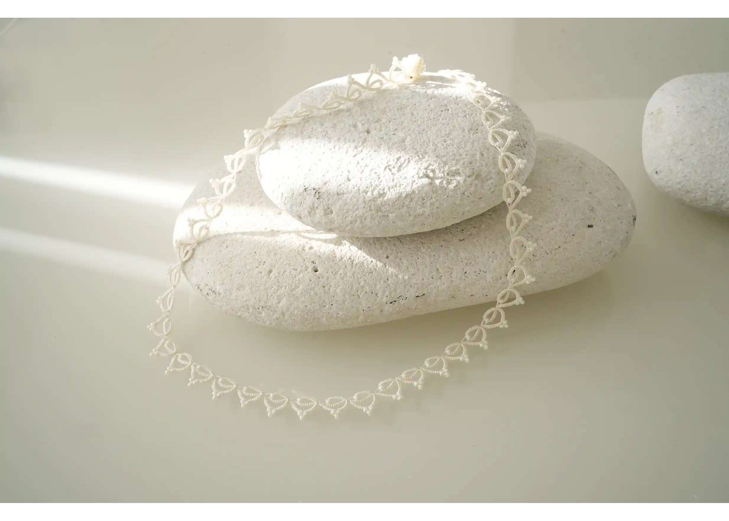 Collier tour de cou fait main en fil et perles, Lotus Chain, photo prise sur un galet