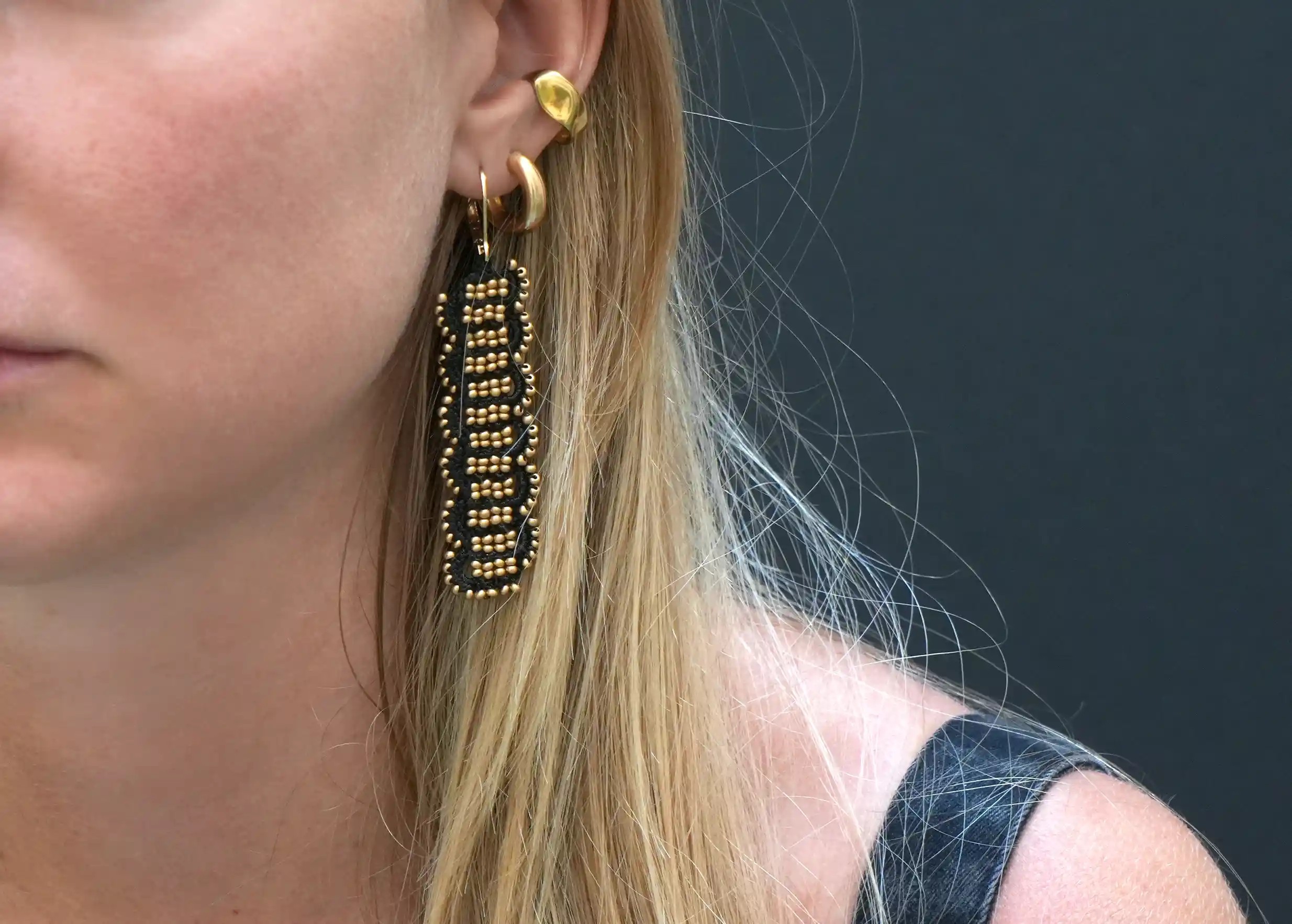 Woman wearing wire and metallic bead earrings, Bark model, black and shiny gold colour