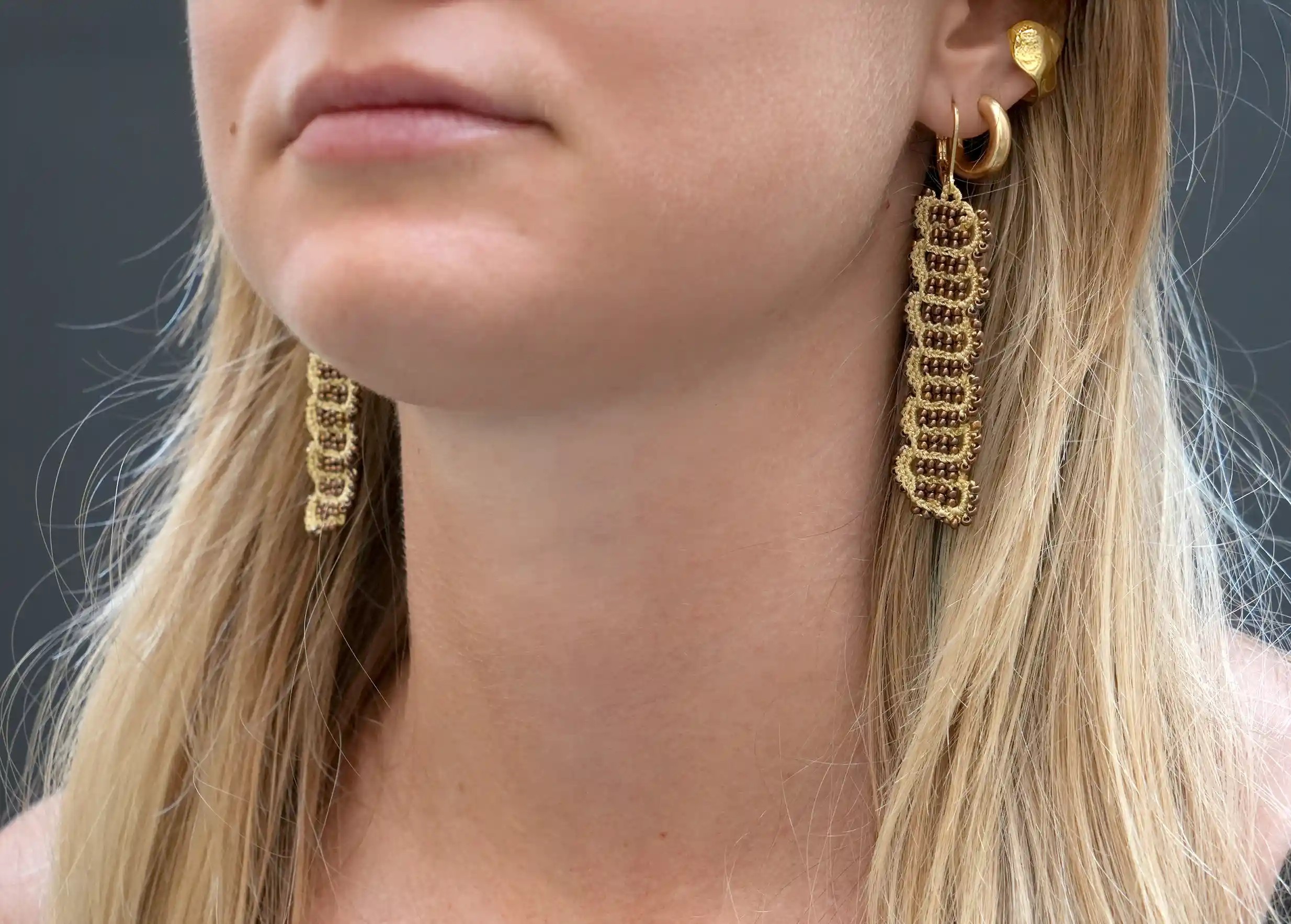 Woman wearing wire and metallic bead earrings, Bark model, gold and dark copper colours