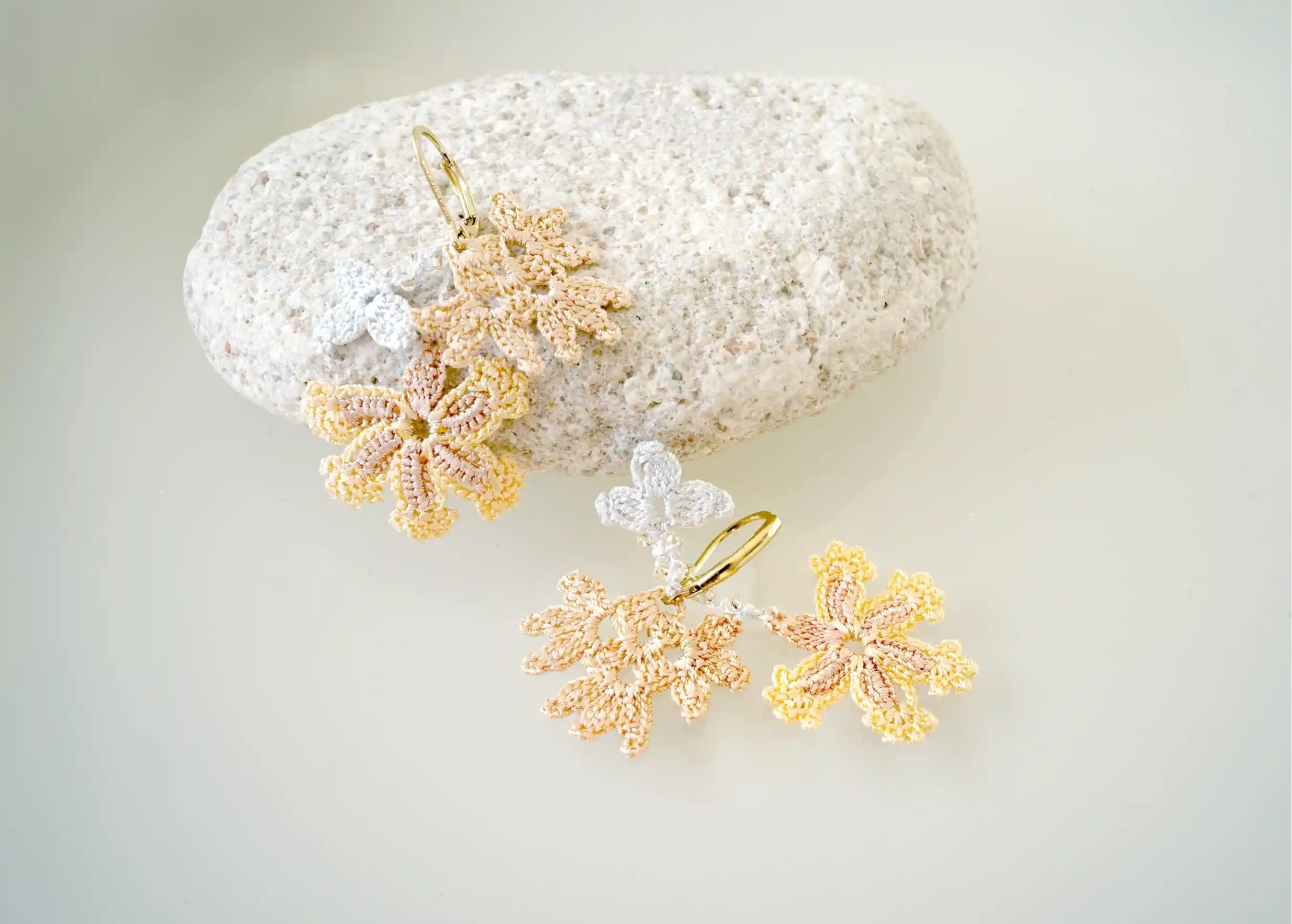 Details of thread lace and pearl earrings, mother-of-pearl colour, photo taken on pebbles