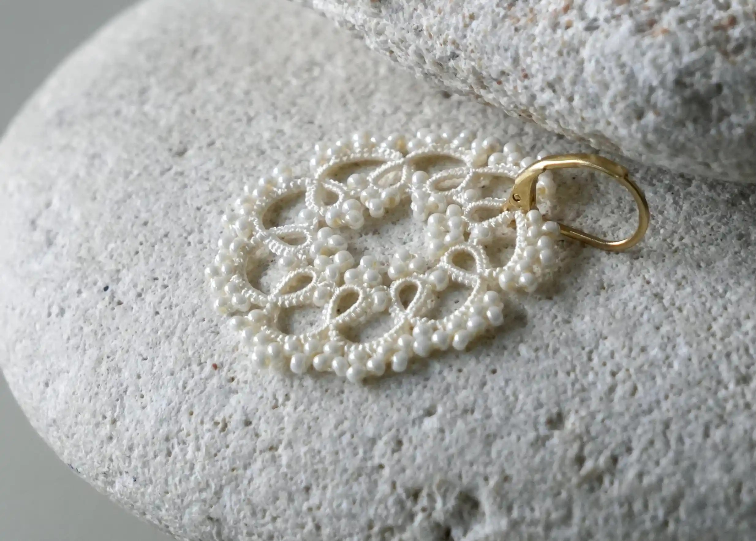 Zoom sur les details des boucles d'oreilles réalisées en fil et perles, au motif géométrique, coloris ivoire clair
