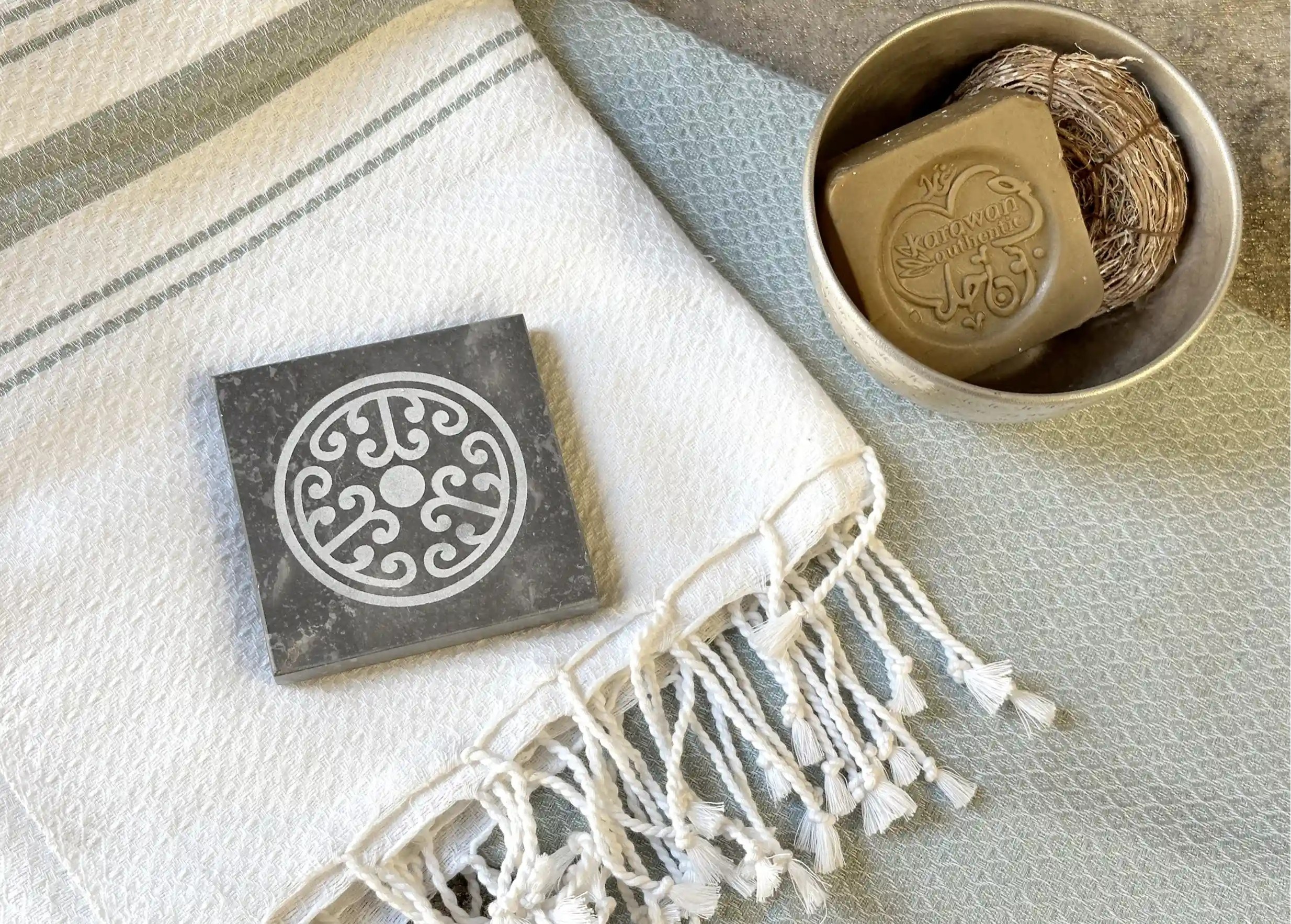 Porte-savon en marbre noir sur une fouta en coton biologique, accompagnée d’un savon d’Alep