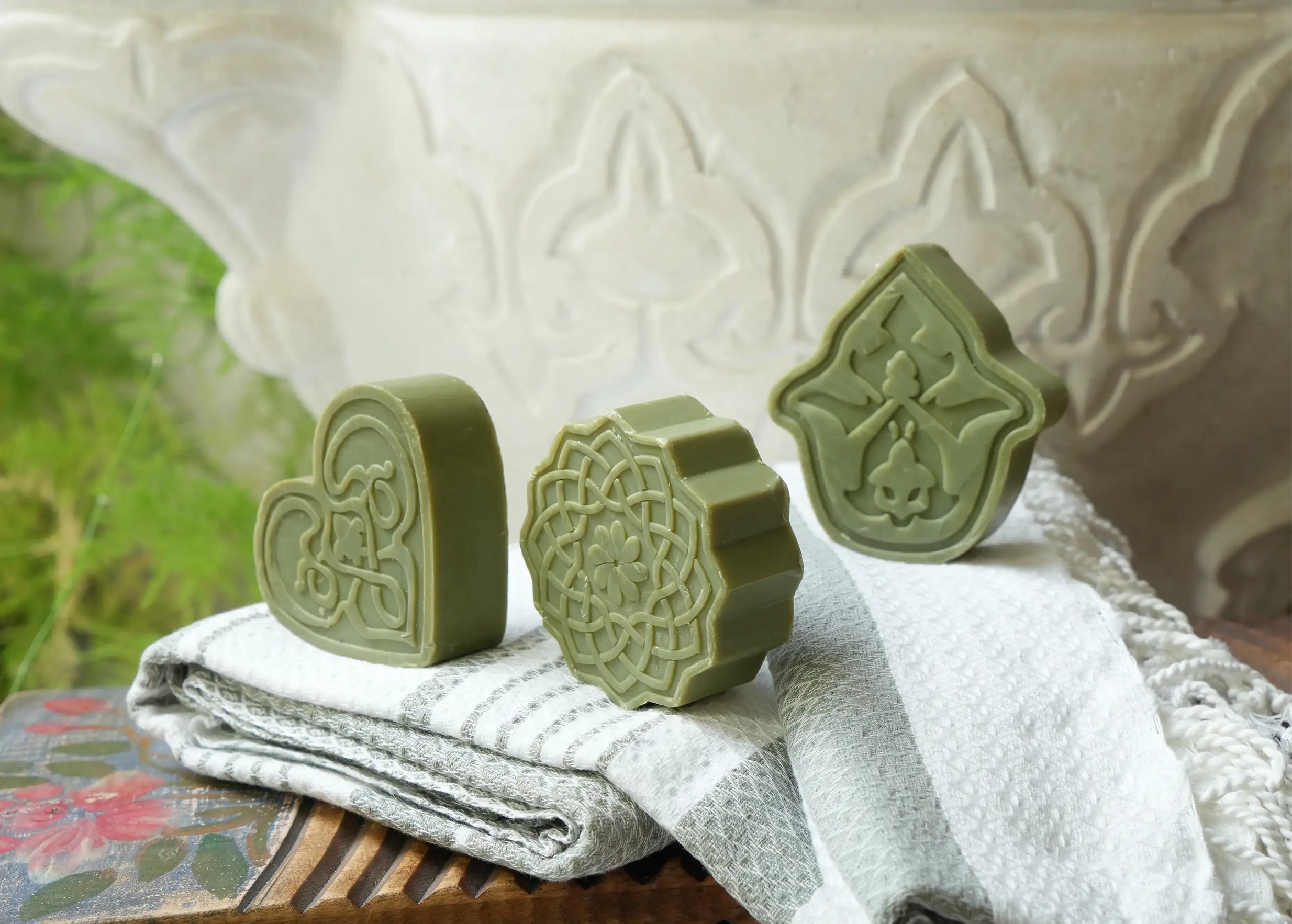 3 savons d'Alep artisanaux en forme de coeur, pétale et fleur, posés sur des foutas en coton biologique