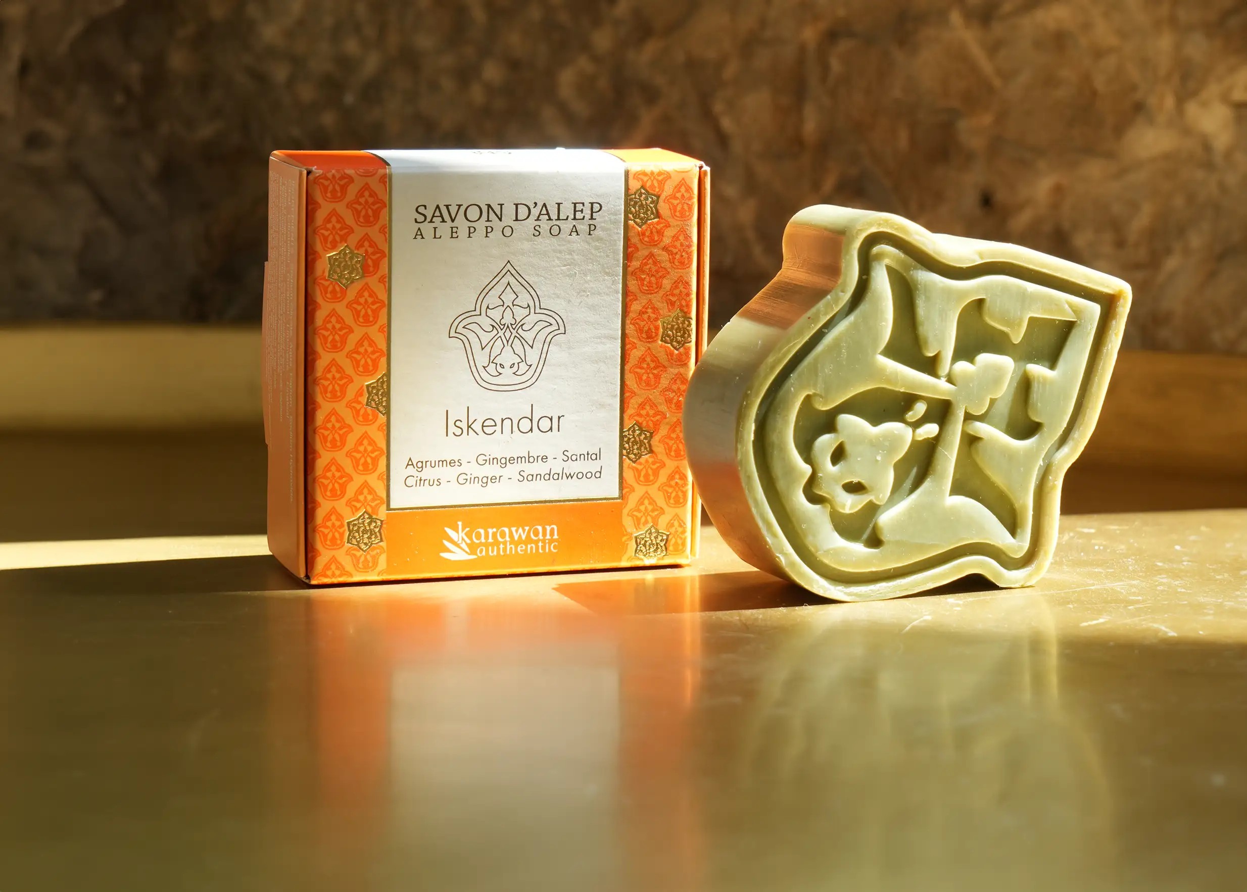 Savon d'Alep parfumé Iskendar, en forme de pétale et à la senteur d'agrumes, à côté de son écrin doré
