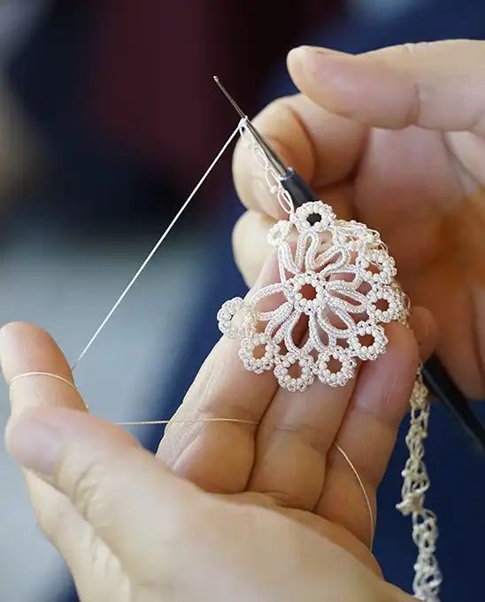 Gros plan d'une main en train de réaliser un bijoux en dentelle turque au crochet. 