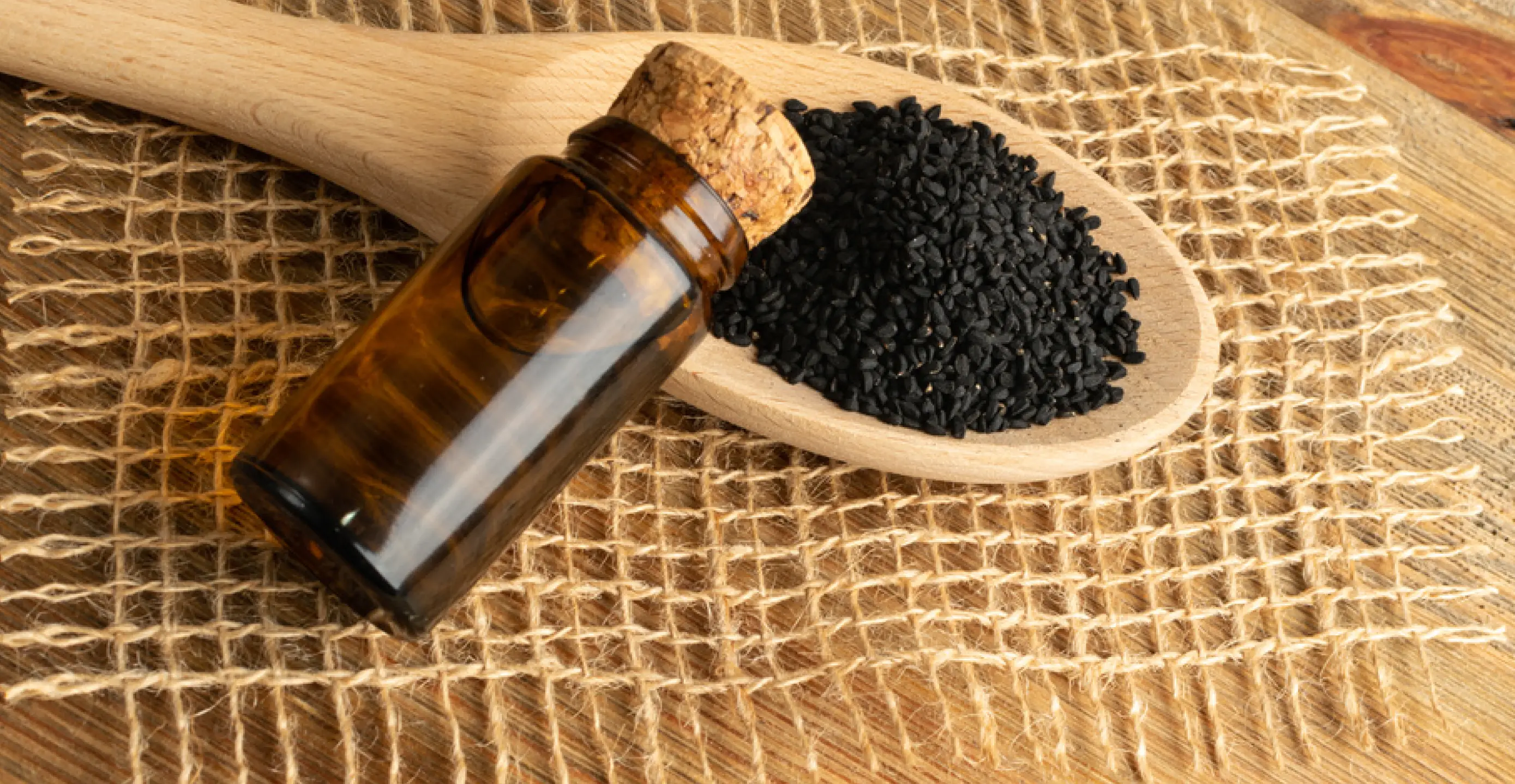 Black cumin oil in a glass flask and nigella seeds on a wooden spoon