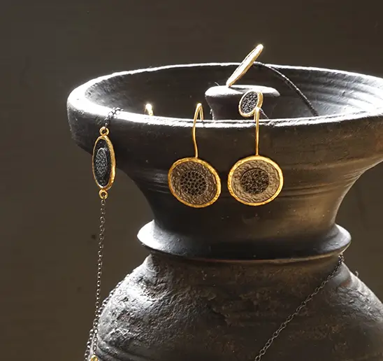 Collection de bijoux en laiton comprenant des bracelets, bagues et boucles d'oreilles, présentés à la paroi d'un vase