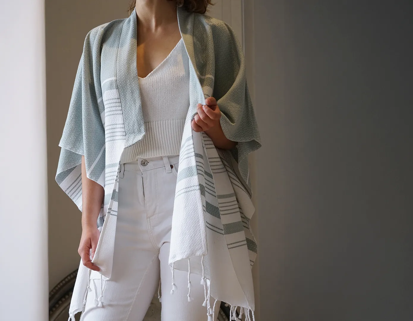 Femme portant un kimono en coton bio Bleu Mirage, se tenant près d’une grande fenêtre avec des rideaux blancs